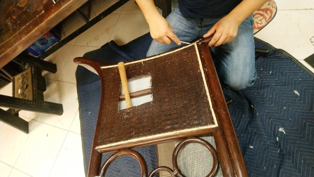 Craftsman removing damaged cane from a McGuire cane dining chair in the workshop before restoration.