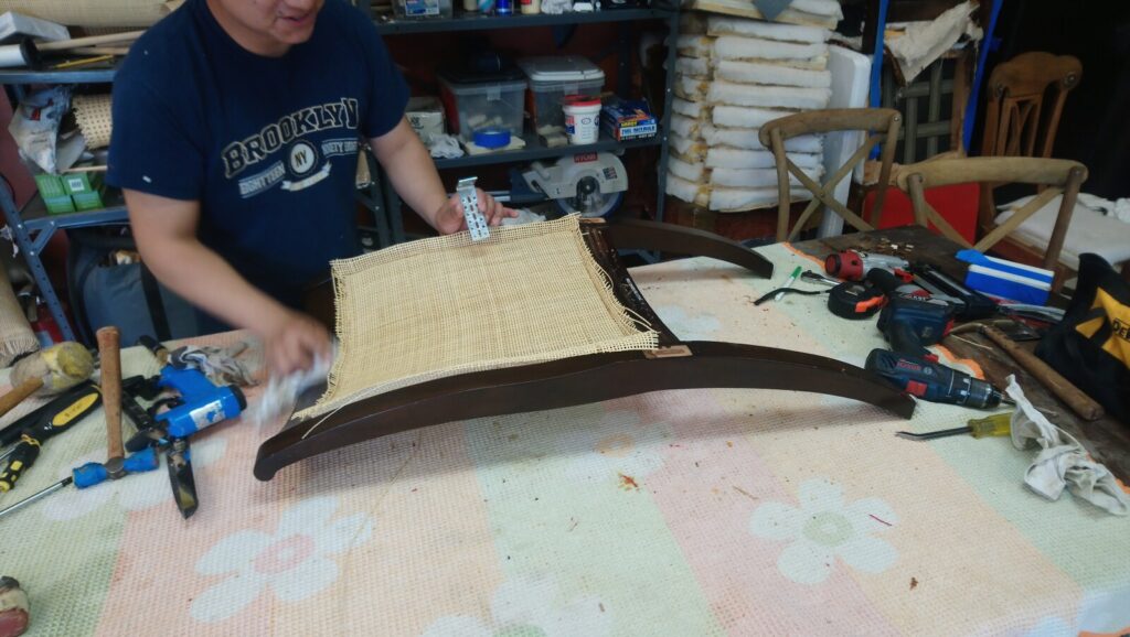 Craftsman installing new cane on the back of a McGuire cane dining chair during the restoration process.