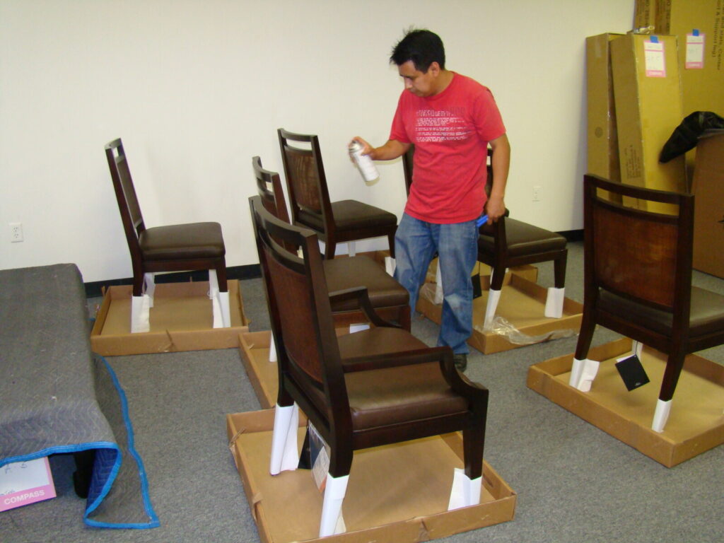Technician spraying lacquer topcoat on McGuire cane dining chairs inside the Baker warehouse finishing room.