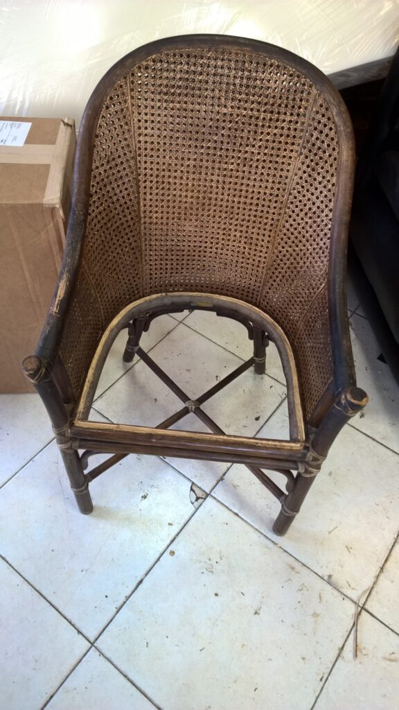 McGuire cane‑panel armchair with the damaged cane fully removed, shown in the workshop before restoration.