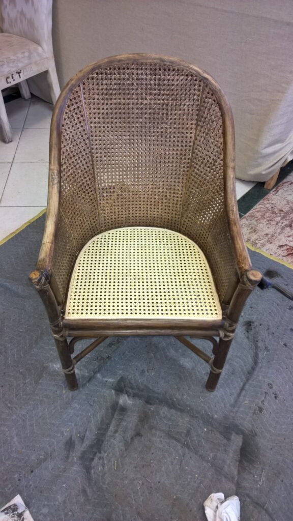 Craftsman installing new cane on a McGuire cane‑panel armchair during the replacement process in the workshop.