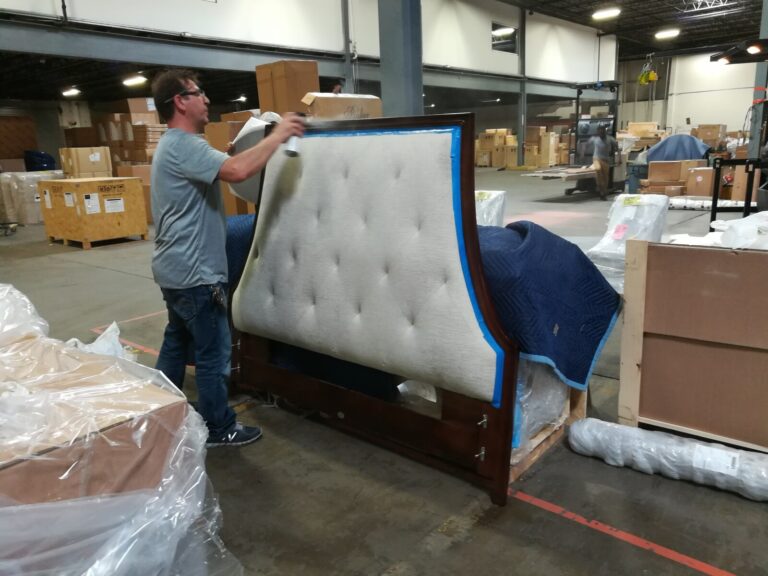 Craftsman spraying a lacquer topcoat on a Baker headboard inside the Baker warehouse during the restoration process.