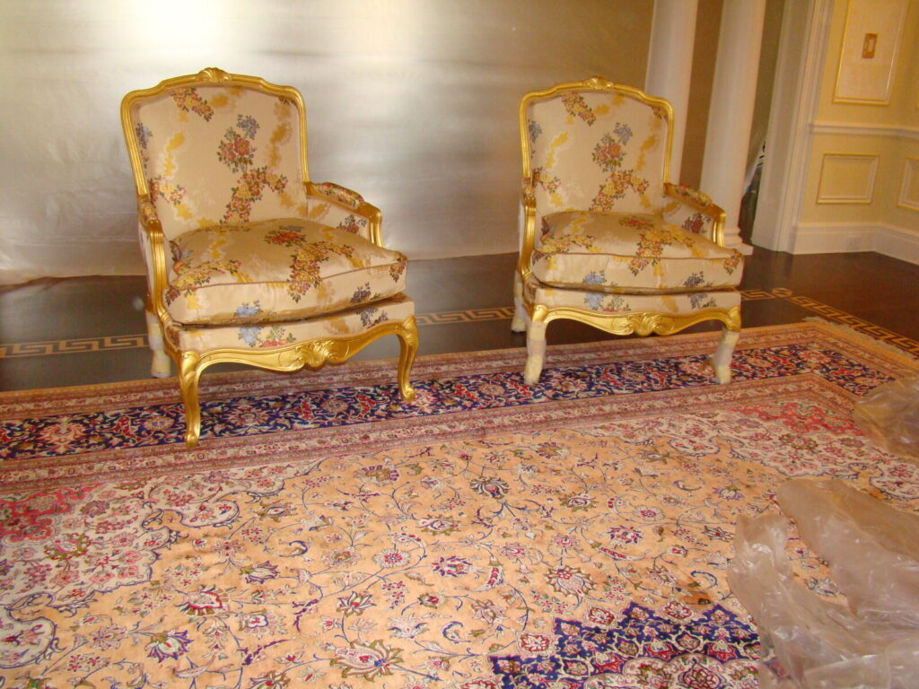 Pair of Baker Louis XVI–style gilded armchairs with tapestry upholstery shown after delivery.