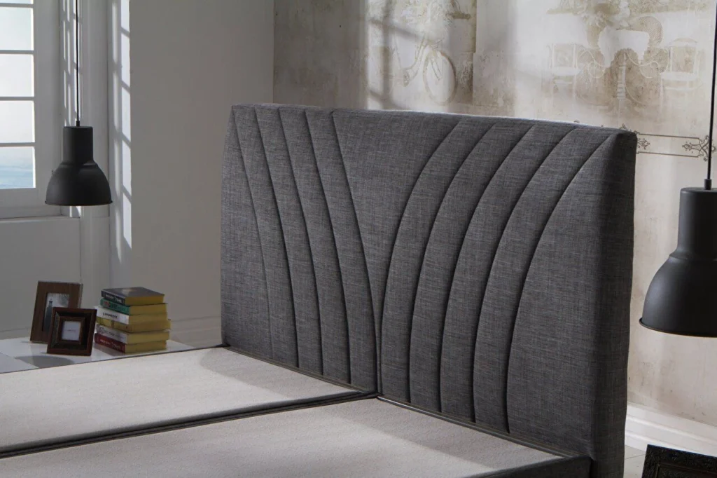 Modern bedroom with a curved dark gray upholstered headboard, split bed base, and black pendant lights.