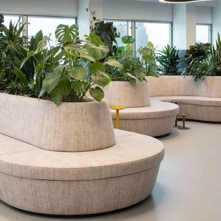 “Modern indoor seating area with circular upholstered banquettes and benches featuring built‑in planters filled with lush green plants.