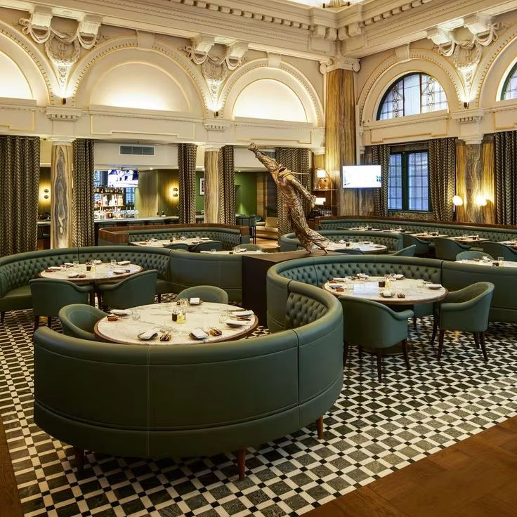 Upscale restaurant interior with curved green leather banquettes, circular tables, and ornate architectural details.