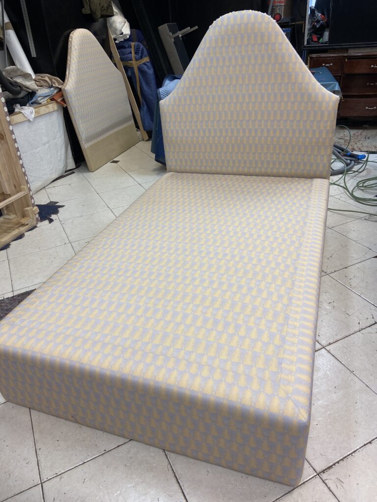 Custom upholstered twin platform bed featuring a pointed arched headboard and matching patterned fabric in the workshop.