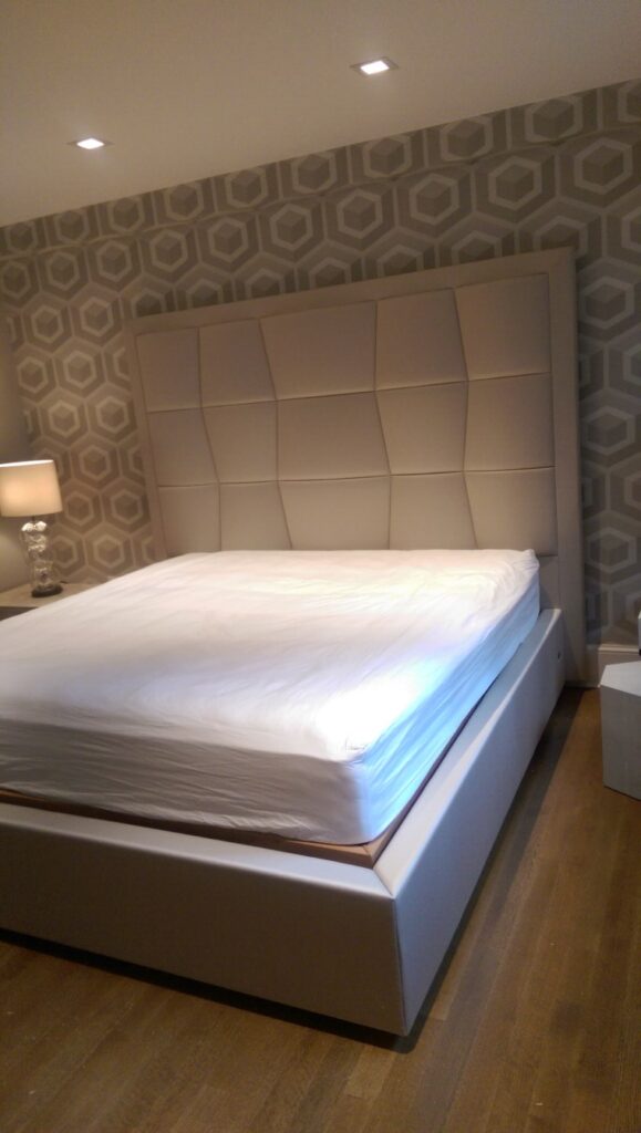 Gemini said Custom upholstered cream leather headboard featuring a geometric block-tufted design, framed and set against a hexagonal pattern wallpaper.