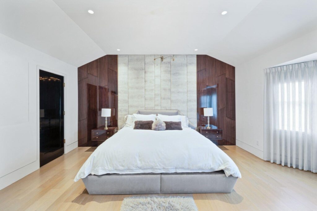 Modern bedroom featuring vertical fabric wall panels flanked by high-gloss wood accents, a grey velvet bed, and gold lamps.