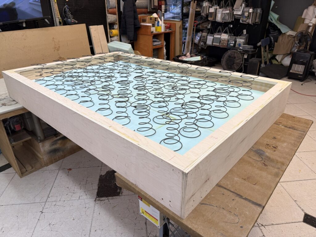 Custom bed frame in bare wood with an 8‑way hand‑tied coil spring base installed during fabrication.