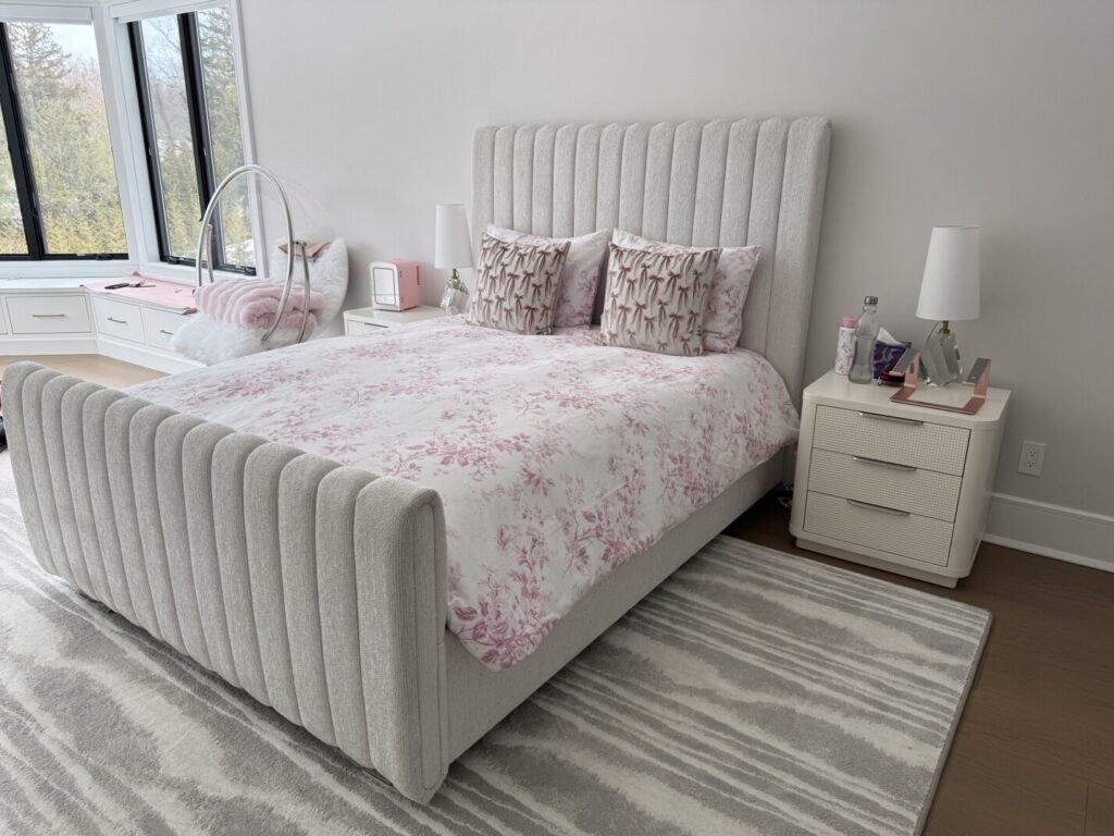 Bedroom with a tall channel‑tufted upholstered headboard, matching bench, nightstands with lamps, and a hanging bubble chair by the window.