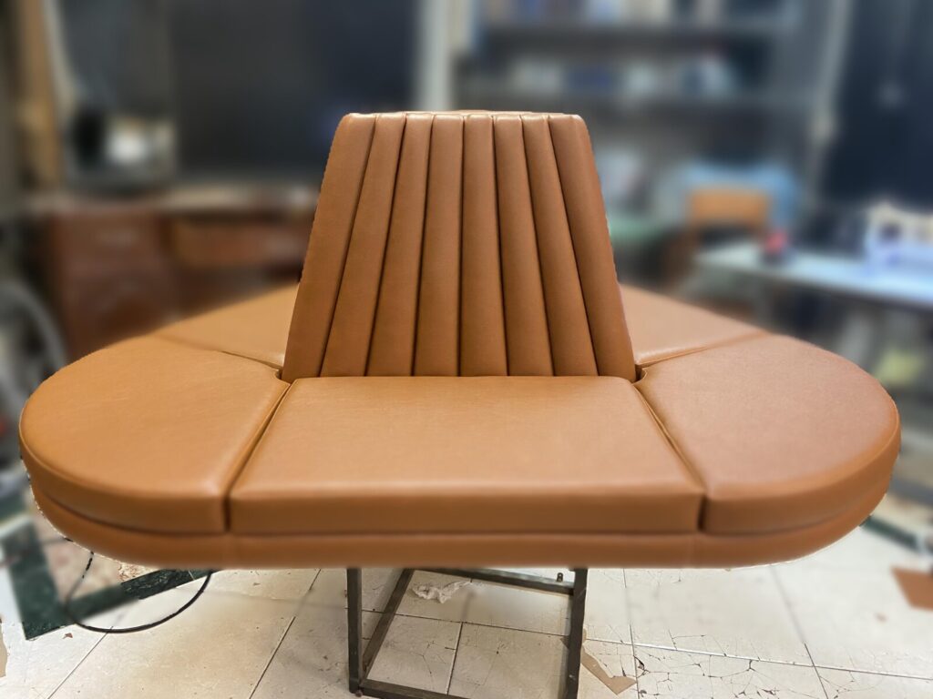 Curved banquette frame clamped on a workbench in the upholstery shop.