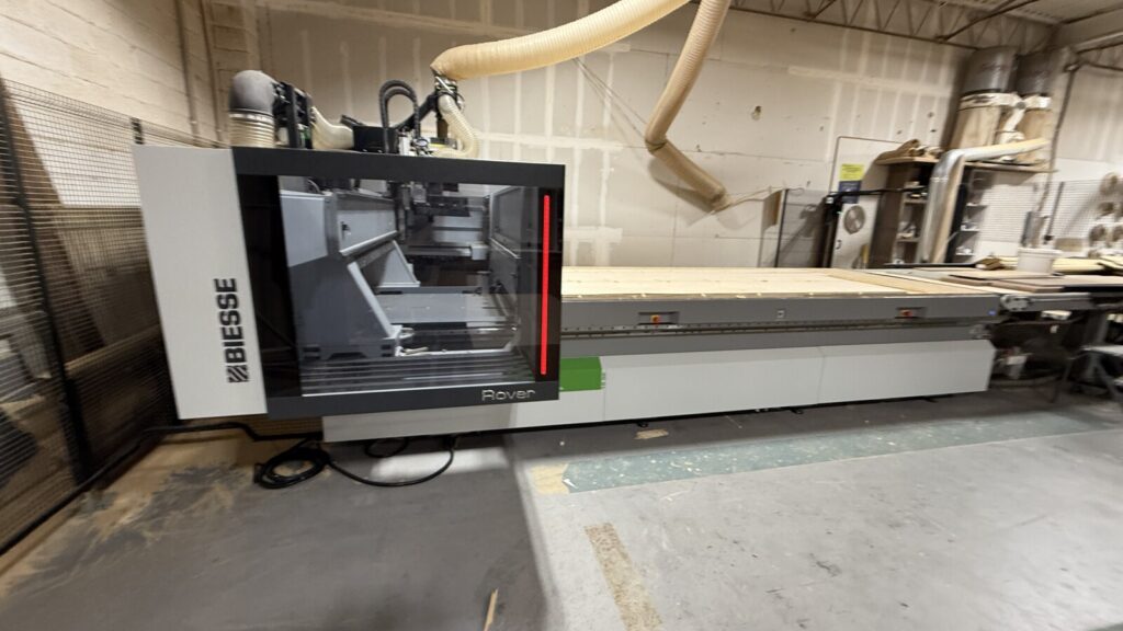 Biesse Rover CNC machine in the workshop, showing the enclosed cutting head, worktable, and dust‑collection system.