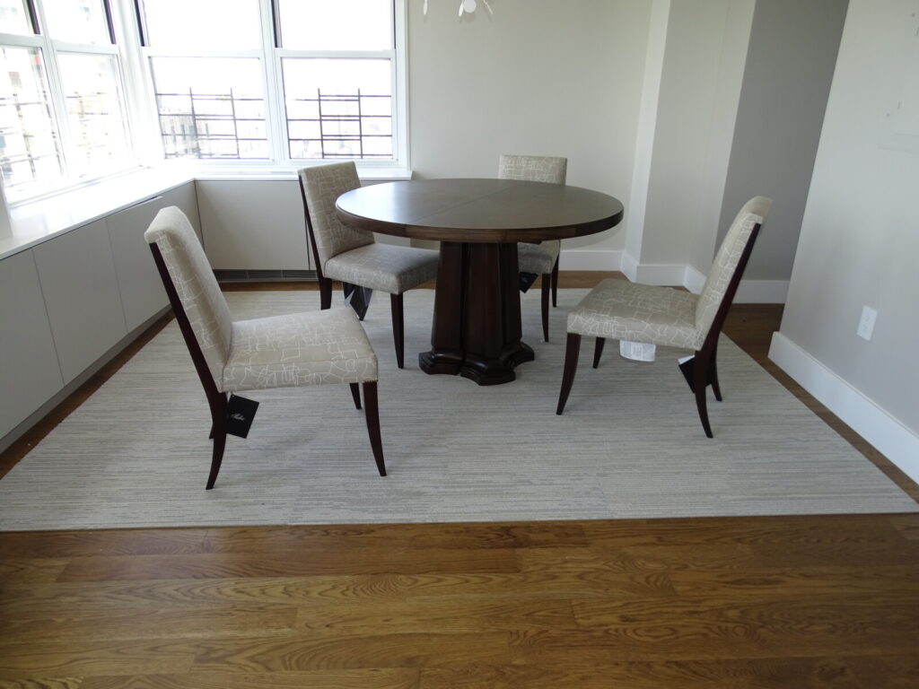 Baker Thomas Pheasant round dining table with four upholstered dining chairs in a sunlit apartment setting.