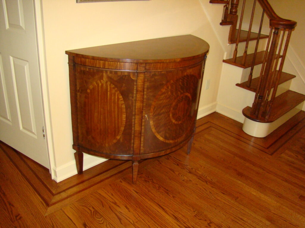 Mahogany cabinet with sunburst inlay restored with veneer repair and refinishing, shown after delivery in a finished interior.