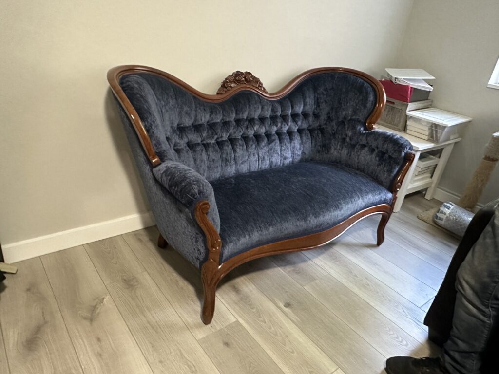 Antique Victorian settee restored with structural repair and reupholstery, shown after delivery in a finished interior.