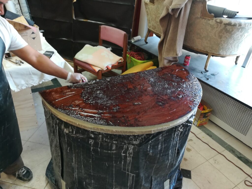 Craftsman stripping a Baker Stately Homes demilune chest in the workshop at the start of the high‑gloss restoration process.