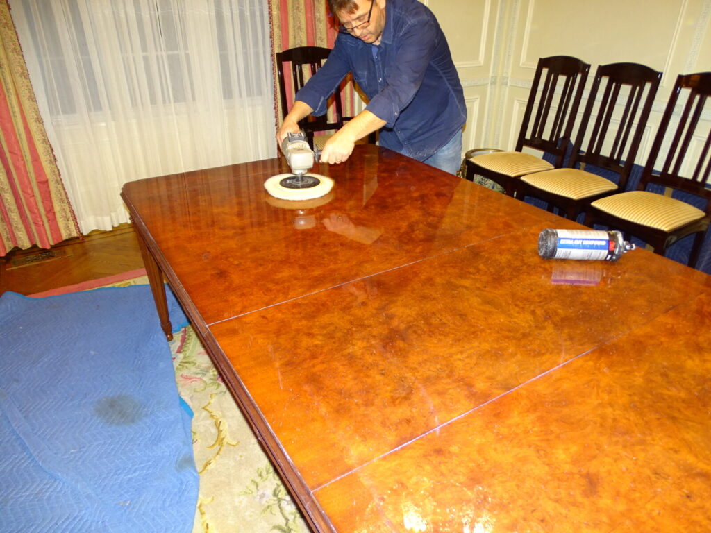 Craftsman polishing a Baker Louis XVI mahogany dining table on‑site in the client’s NYC home to remove surface scratches before refinishing.