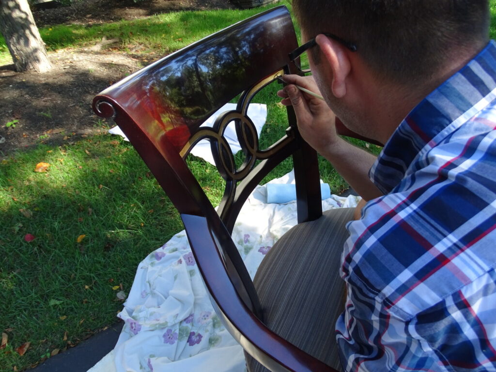 Touching up gold leaf on an antique chair in the client’s backyard during on‑site restoration.
