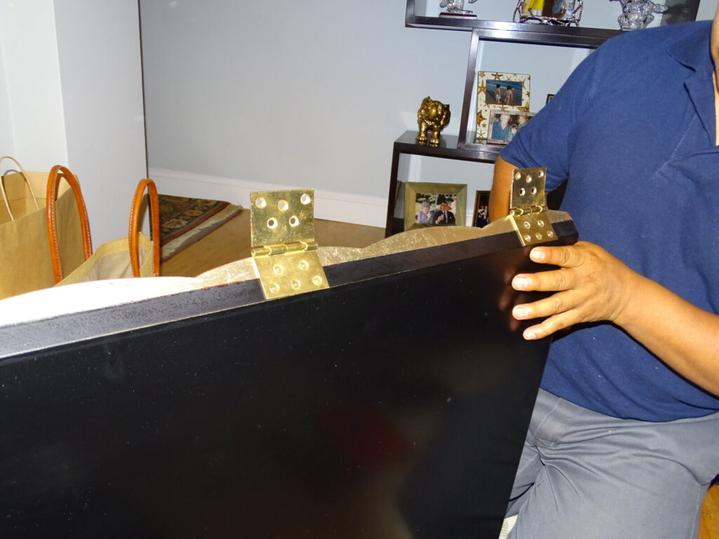 Inspecting a gold‑leaf diamond chest in the client’s home, showing damaged hinges and finish before restoration.