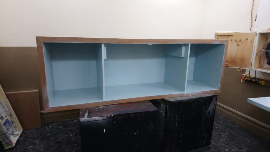 Baker sideboard stripped to bare wood in the workshop, showing the antique gold exterior and light‑blue interior before refinishing.