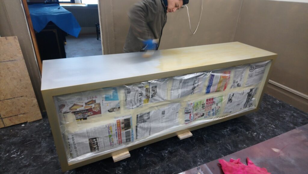 Baker sideboard in the workshop before refinishing, showing the antique gold exterior and light‑blue interior during the initial inspection stage.
