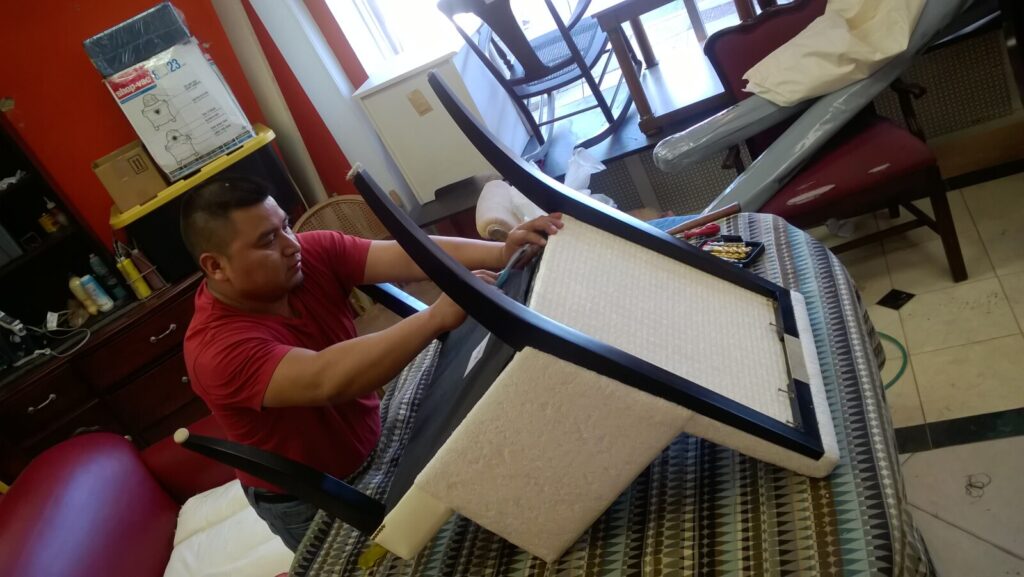 Baker Thomas Pheasant Atelier side chair with factory‑installed wrong fabric, photographed in the shop before restoration while a craftsman works on the frame