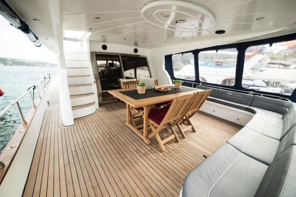 Covered yacht deck dining area featuring custom-fitted grey perimeter seating and teak wood furniture.