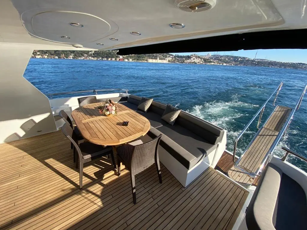 Yacht stern deck with custom charcoal grey upholstery, outdoor dining table, and teak wood flooring overlooking the water.
