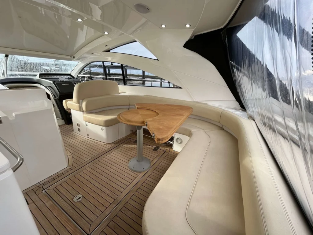 Luxury yacht helm area with custom cream-colored marine upholstery, teak wood flooring, and a unique wood-topped folding table.