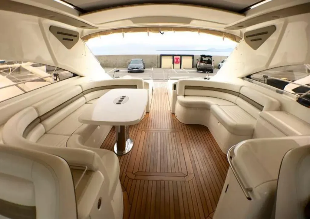 Covered yacht aft deck with expansive custom-fitted white marine upholstery, outdoor dining area, and teak wood flooring.