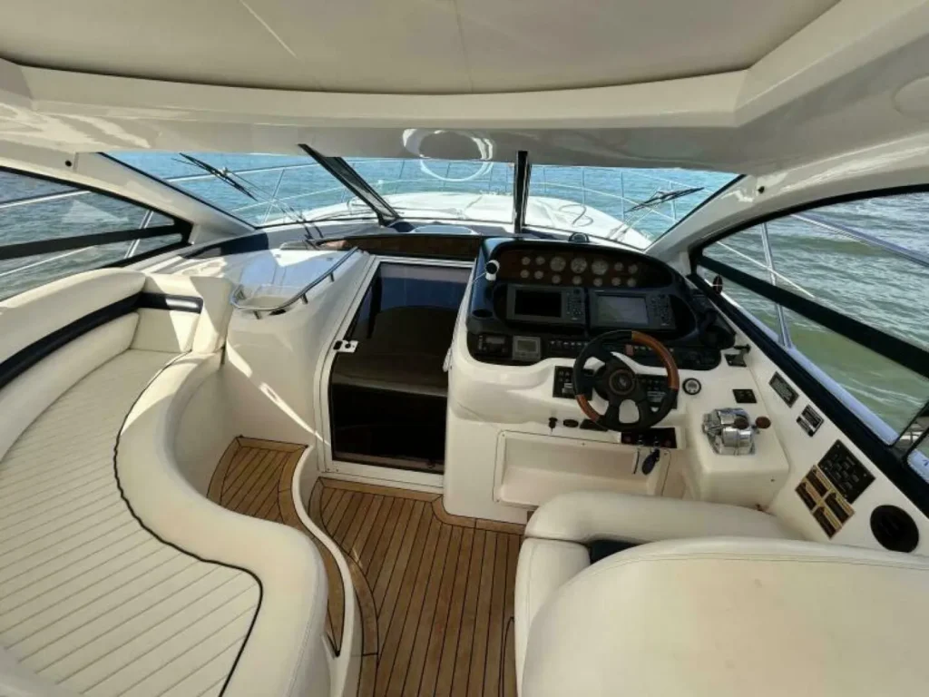 Modern yacht cockpit featuring custom white marine upholstery with black piping, a comprehensive helm station, and teak wood flooring.