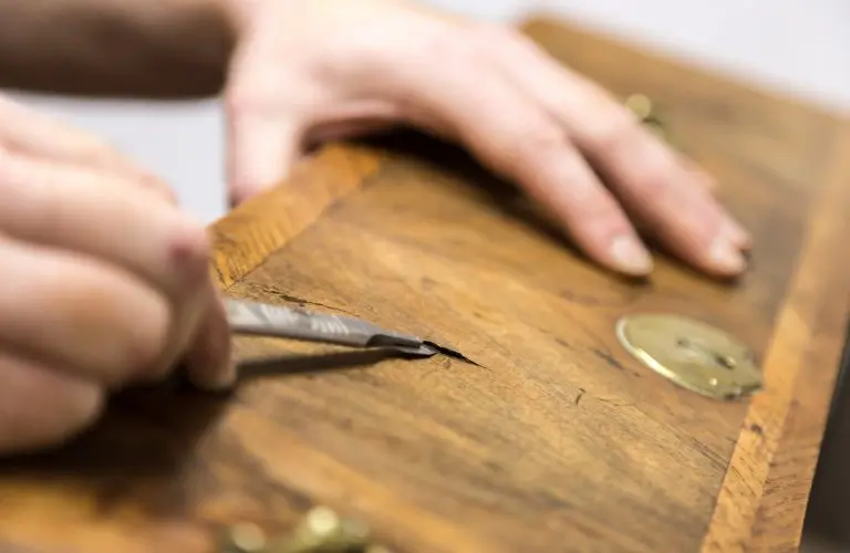 Craftsman repairing damaged veneer on an antique furniture piece during detailed restoration work.
