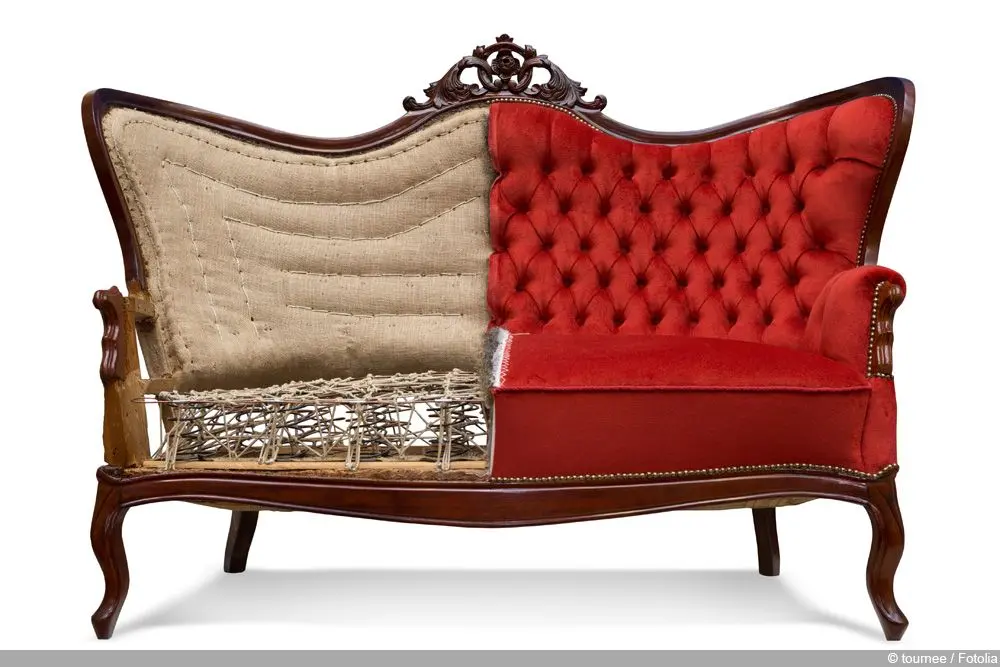 Vintage sofa with half the upholstery removed, showing springs, padding, and internal frame beside the fully upholstered red tufted side.