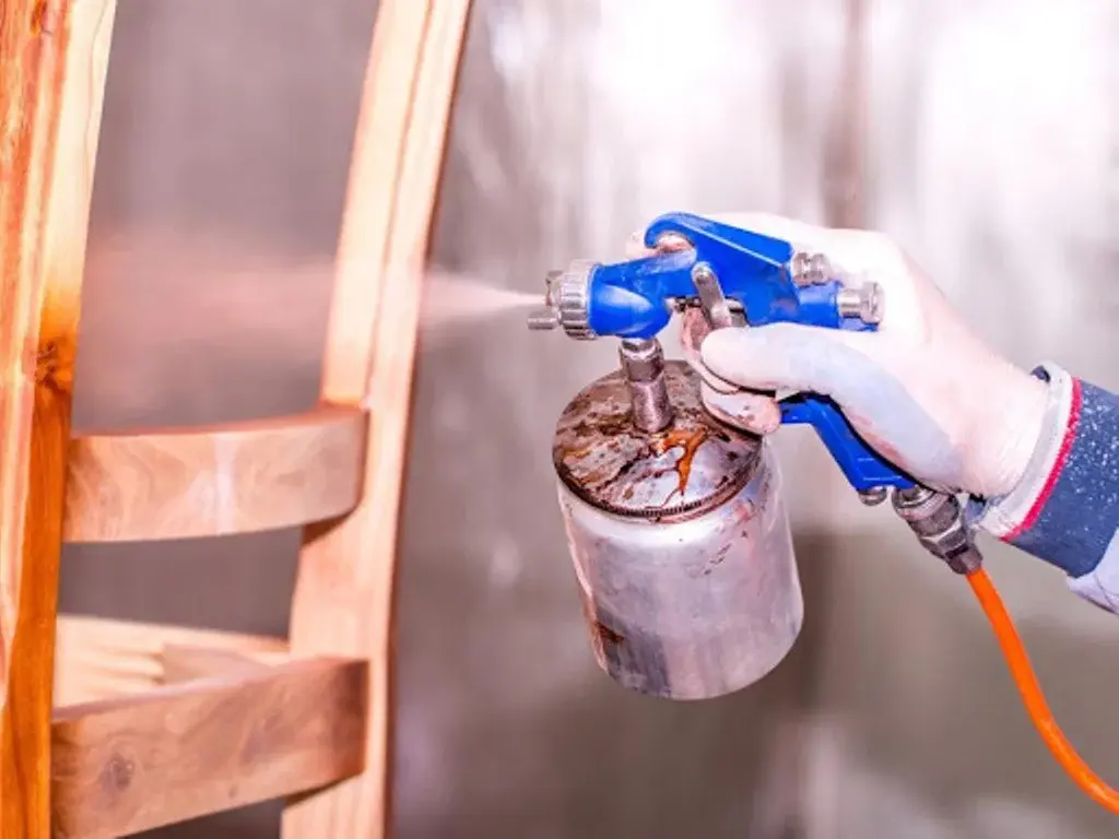 Technician spraying a dining chair in a controlled spray room, applying an even, professional finish.