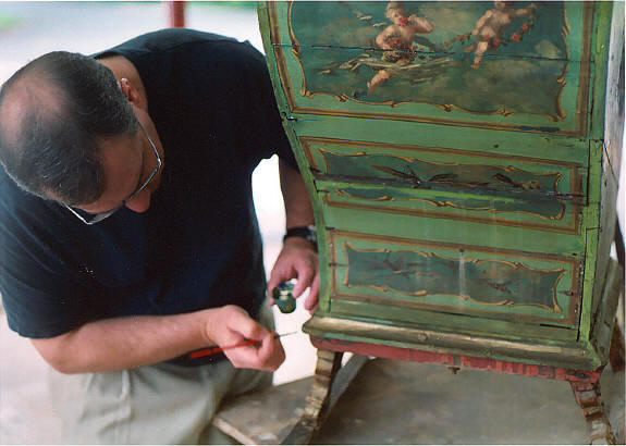 Craftsman touching up a refinished cabinet using detail tools during the final woodwork process.