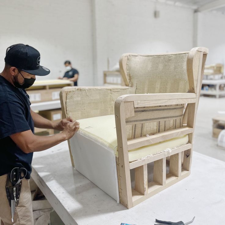 Craftsman adding foam to a bare wooden chair frame at a workbench during early upholstery preparation.