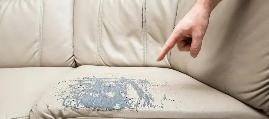 Close‑up of a damaged leather seat cushion with peeling material and a hand pointing to the worn area.