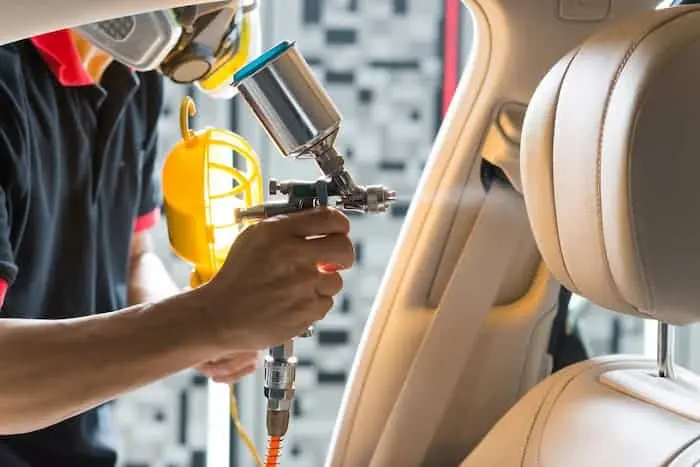 Technician using a spray gun to apply dye or coating to a leather car seat.