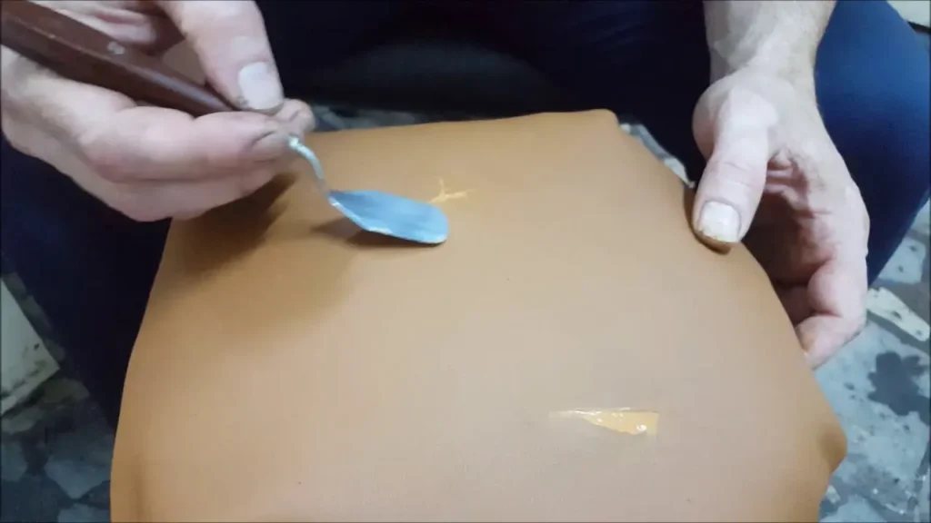 Technician filling a hole in a leather car seat during the repair process.