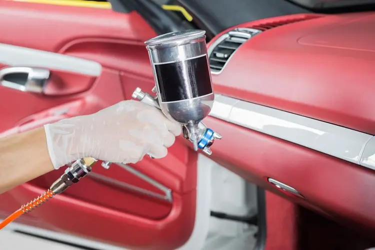 Technician using a spray gun to re‑dye a leather car dashboard.