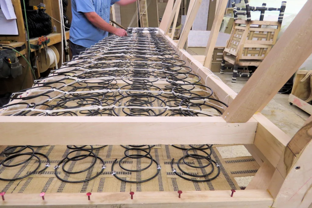 Craftsman tying coil springs with the traditional 8‑way hand‑tied method during the upholstery process.