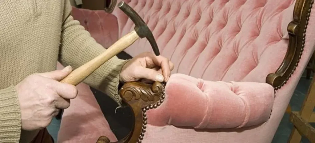 Craftsman stapling fabric to a chair frame in the upholstery workshop during the production process.
