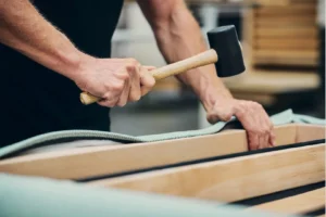 Craftsman removing upholstery tacks from a chair in the workshop during the restoration process.