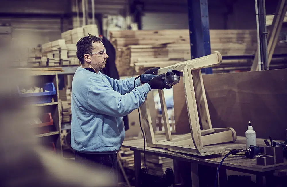 Frame craftsman working at a bench, assembling a wooden furniture frame with tools nearby.