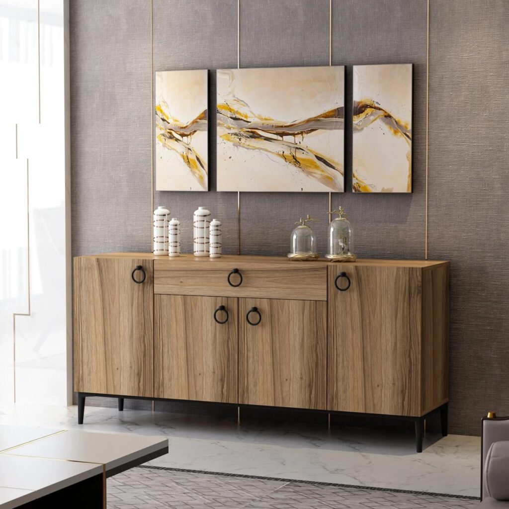 Wood sideboard with black handles beneath a triptych of abstract gold and white paintings, with decorative jars and cloches.