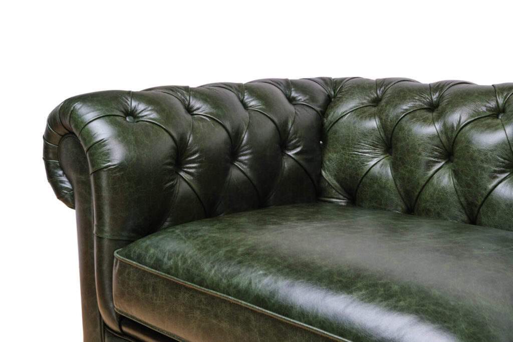 Close‑up of a green leather tufted sofa arm.