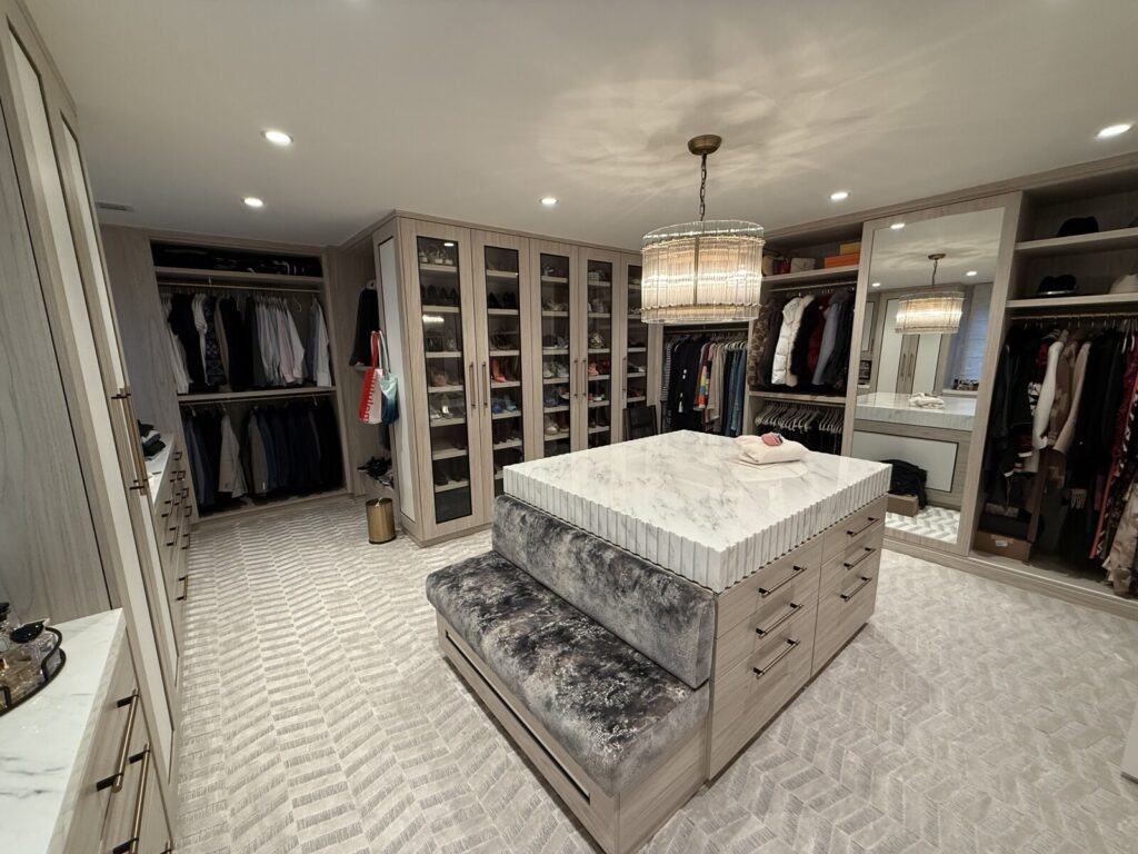 Custom walk‑in closet with a built‑in center island bench upholstered and finished in the client’s home.