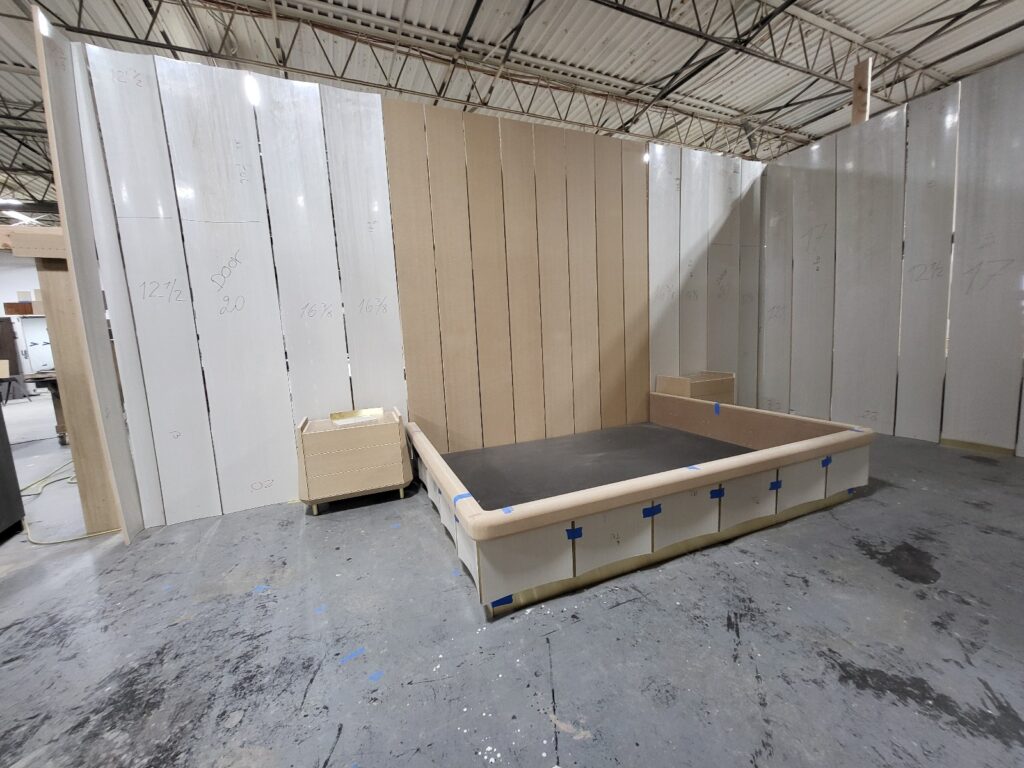 “partially built room mock‑up with tall marked wall panels and a raised platform frame inside a workshop.