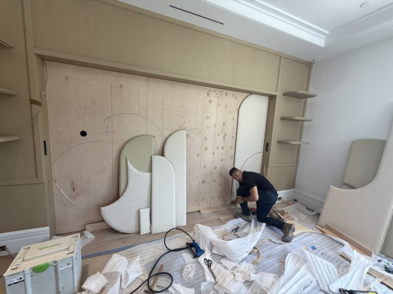 Specialist installing custom upholstered arched panels onto a bare wood wall frame in a luxury bedroom.